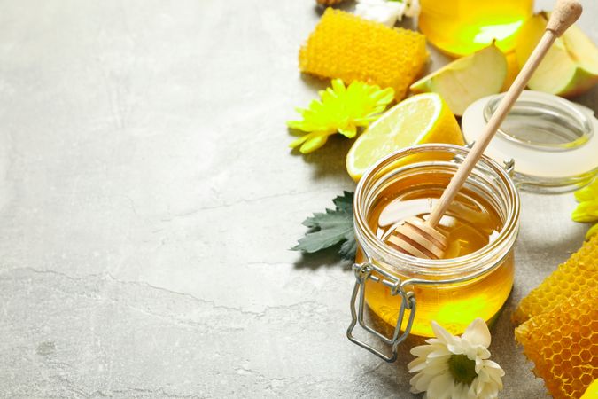 Honey, flowers and fruits on grey background, copy space