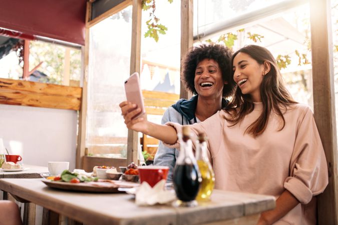 Cheerful woman taking selfie with male friend at college cafe
