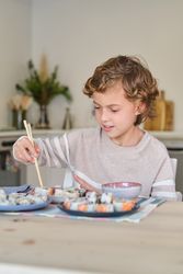 Preteen boy eating sushi with chopsticks