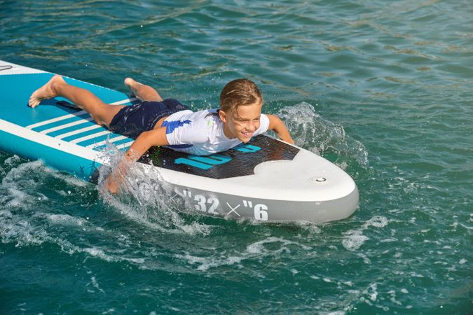 Surfer in wetsuit lying on SUP board and splashing waves