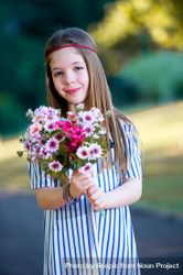 Smiling girl in blue striped dress holding a bouquet of flowers standing outdoor 48EgJb