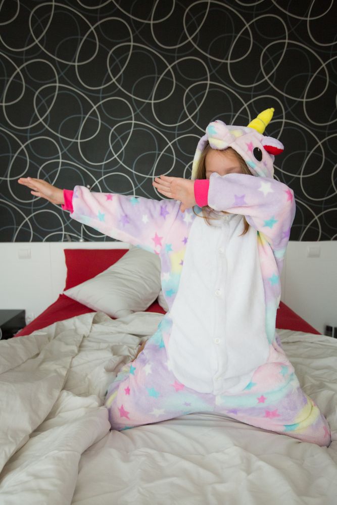 Cheerful girl in unicorn pajama having fun on bed