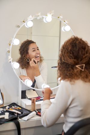 Cheerful woman doing makeup near mirror