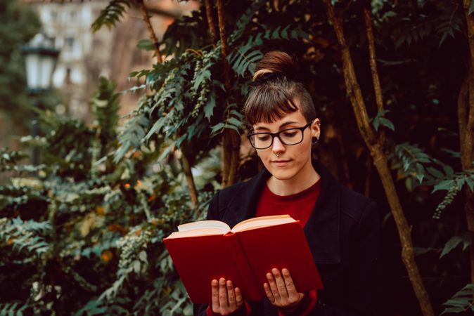 Young woman reading book on bench in park
