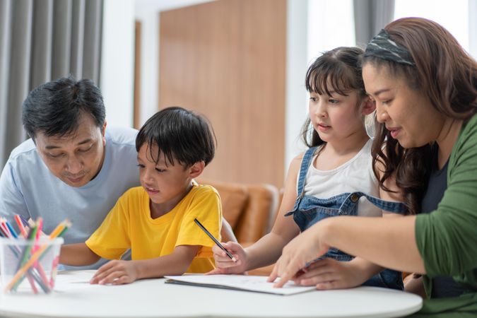 Asian parents helping kids to do homework on table at home