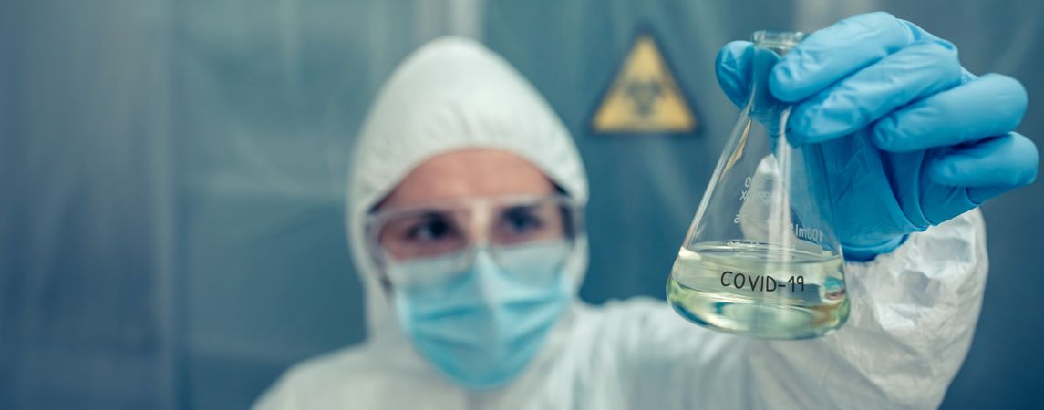 Scientist with protection suit looking test tube in the laboratory