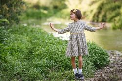 Girl in dress looking away from the river with her arms open