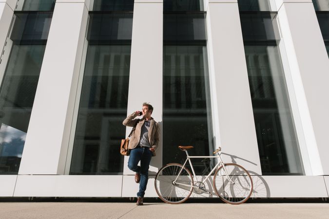 Businessman with smartphone leaning on building on city street