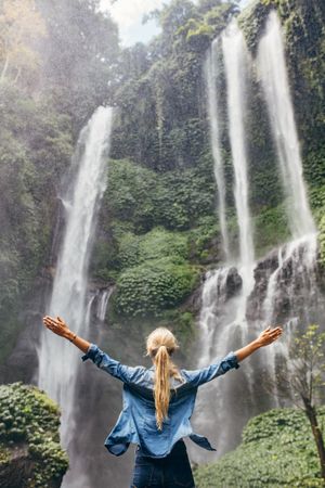 Female tourist with her arms outstretched looking at waterfall