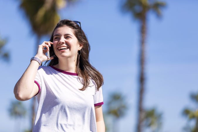 Smiling woman wearing clothes standing outdoors in the street while chatting on a mobile phone on a sunny day