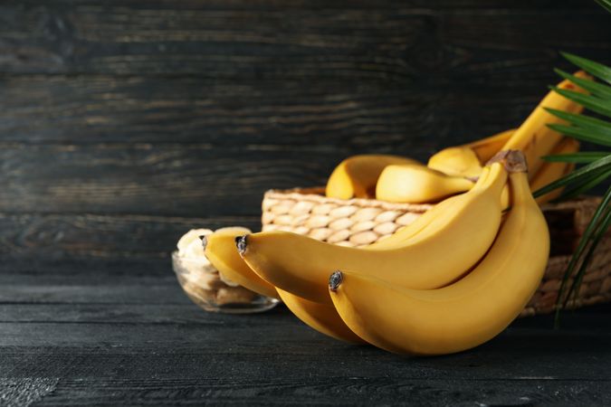 Bananas. Basket with bananas and bowl with slices on wooden background