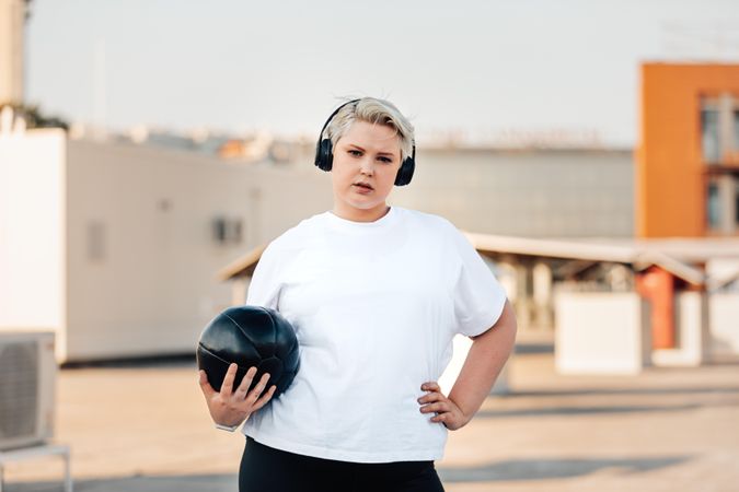 Blonde woman with hand on hip and medicine ball on a rooftop