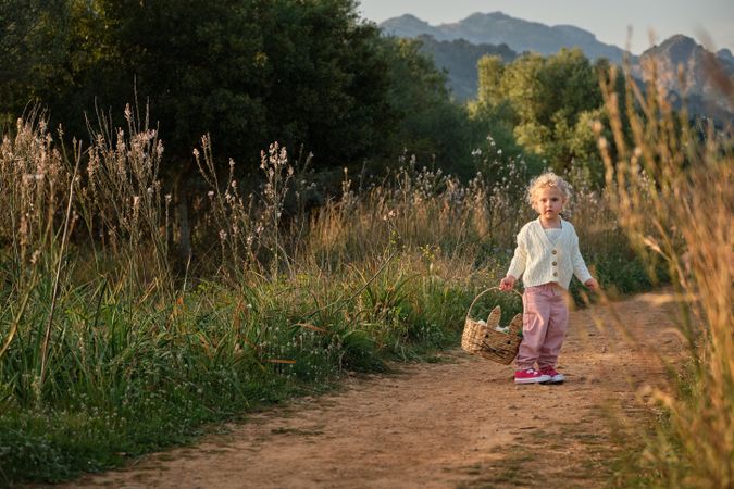 Funny little girl with basket standing on rural road