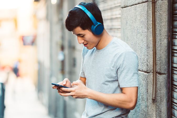 Content Asian man in headphones listening music on smartphone on street