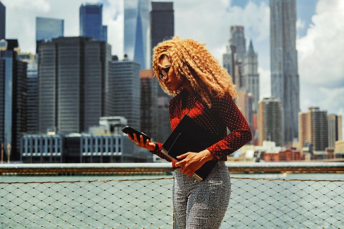 Serious professional Black female checking phone with New York in the background