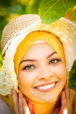 Portrait of woman in yellow hijab and straw hat smiling