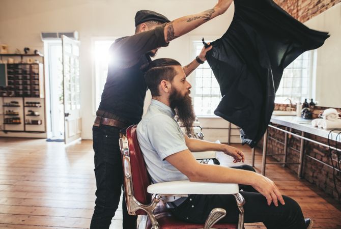 Barber adding cape to male customer in barbershop