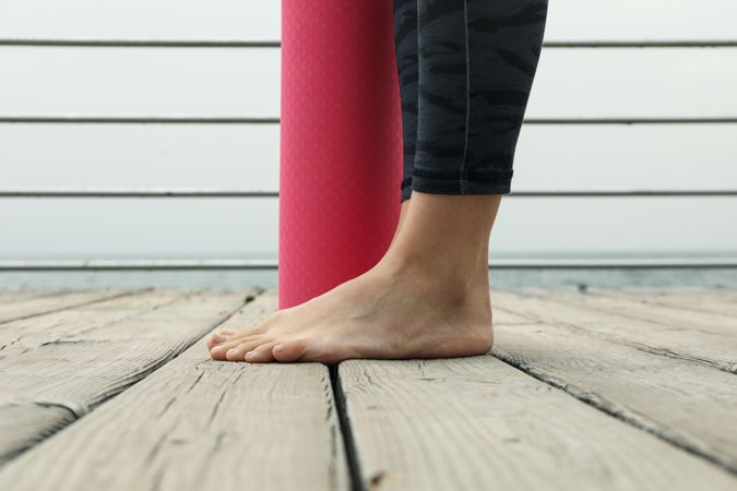 Female legs and pink yoga mat on wooden floor outdoors, close up
