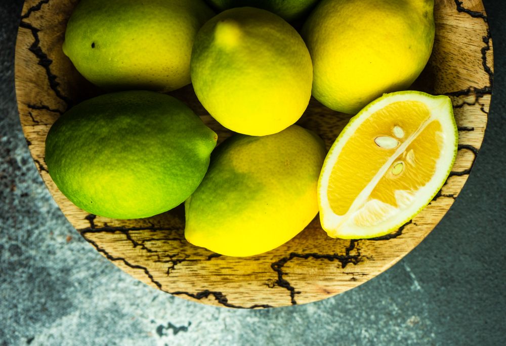 Top view of bowl of fresh lemons with one halved on top