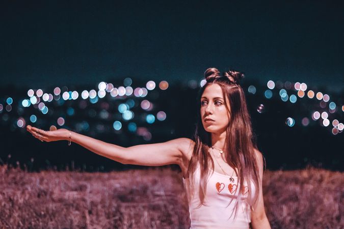 Woman spreading an arm standing on brown grass field at night