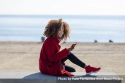 Side view of female checking smart phone on bench on a beach 4j2lJ4