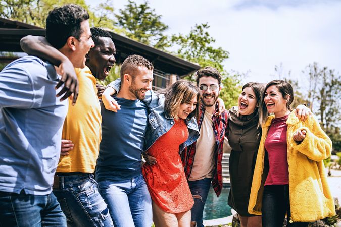 Seven friends, diverse in ethnicity, laugh and stand united in a park