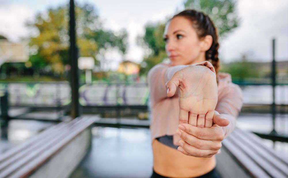 Young female athlete stretching hands and wrists outdoors