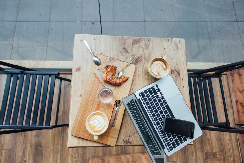 Top view of empty cafe table with laptop, pastry and cappuccinos