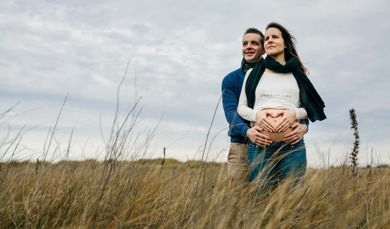 Pregnant woman making heart with hands on naked belly with partner