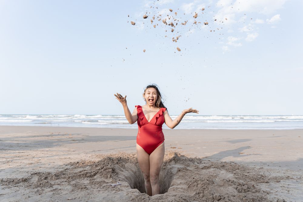 A young Hispanic woman throwing sand to the sky while making a hole playing in the beach