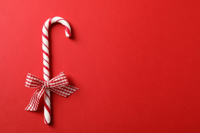Sweet candy cane with bow on red background, space for text