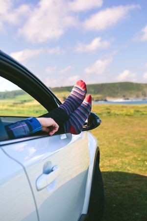 Unrecognizable man resting feet up sitting on the car