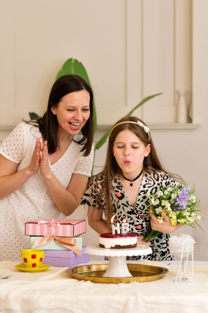 Mother and daughter celebrating birthday, with girl blowing out candles