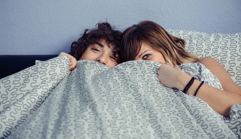 Happy couple playfully hiding under duvet