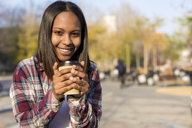 Happy female in plaid shirt holding a to go coffee