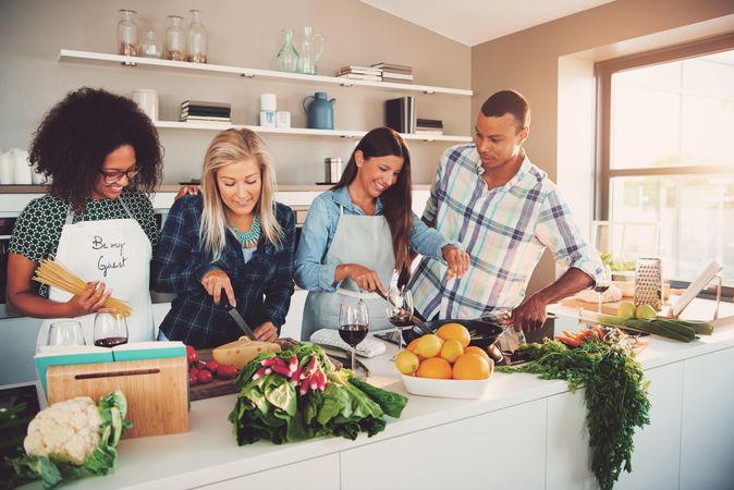 Multi-ethnic group of friends prepping vegetables and pasta in a bright kitchen