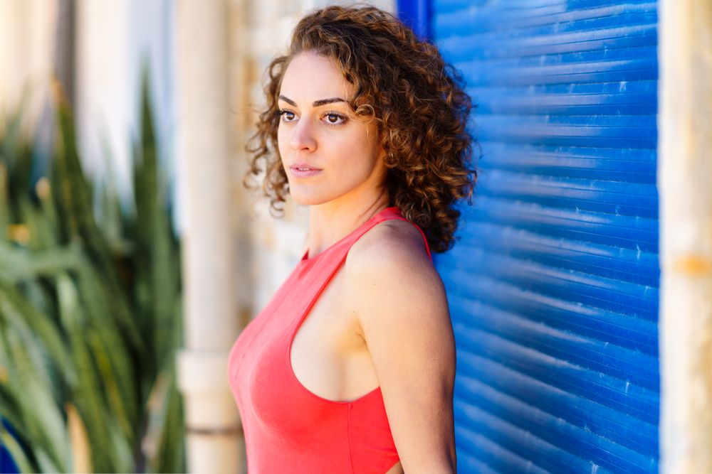 Side view of serious woman standing in front of blue shutters in red vest