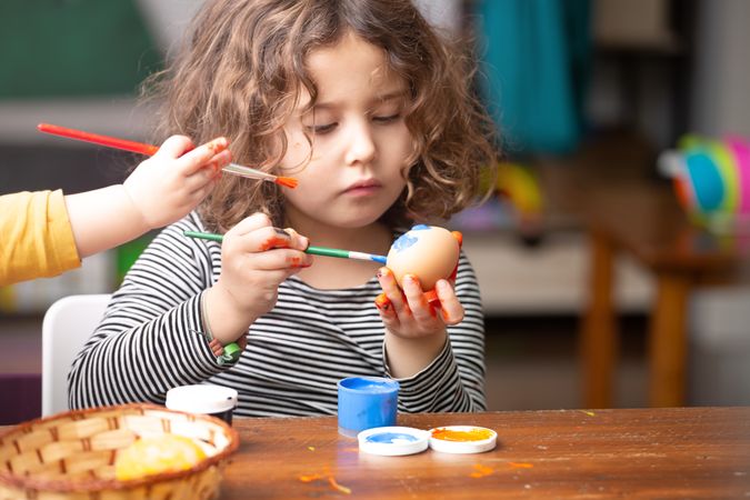 Toddler girl painting egg at table