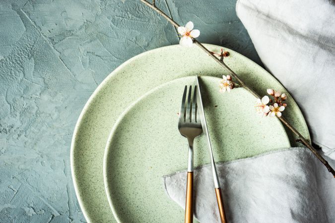 Top view of silverware on spring table setting blooming tree branch on grey table