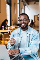 Delighted Black man with coffee browsing laptop
