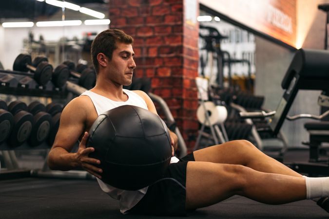 young man doing weight ball abs exercise in a gym