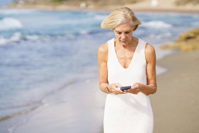 Older woman using her phone on a rocky beach