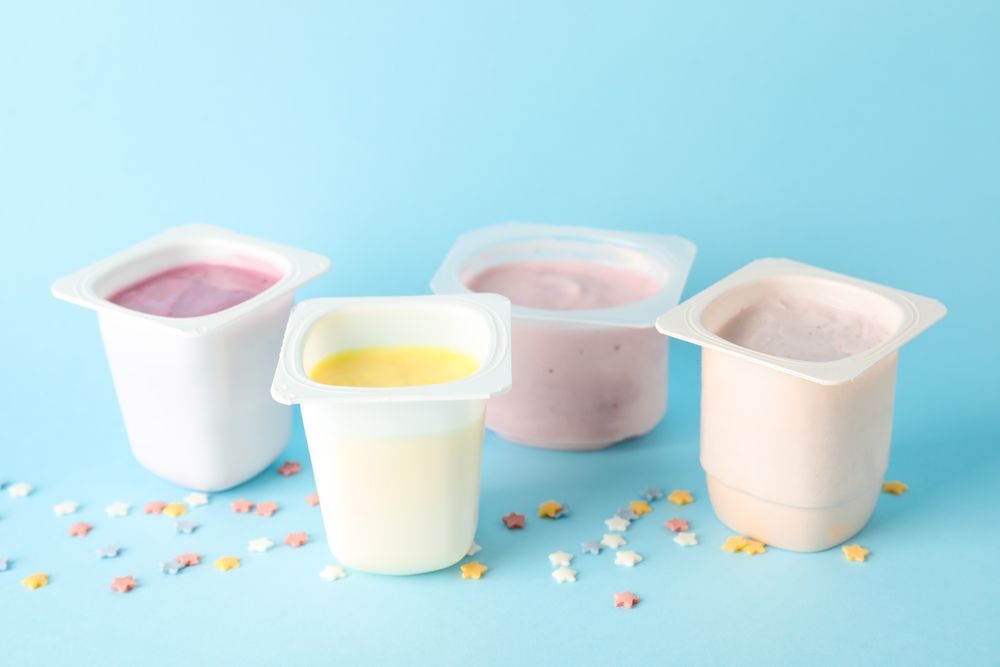 Plastic cups with yogurt and small stars on color background, space for text