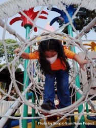 Girl with facemask standing in a climbing net at the playground 5rK874