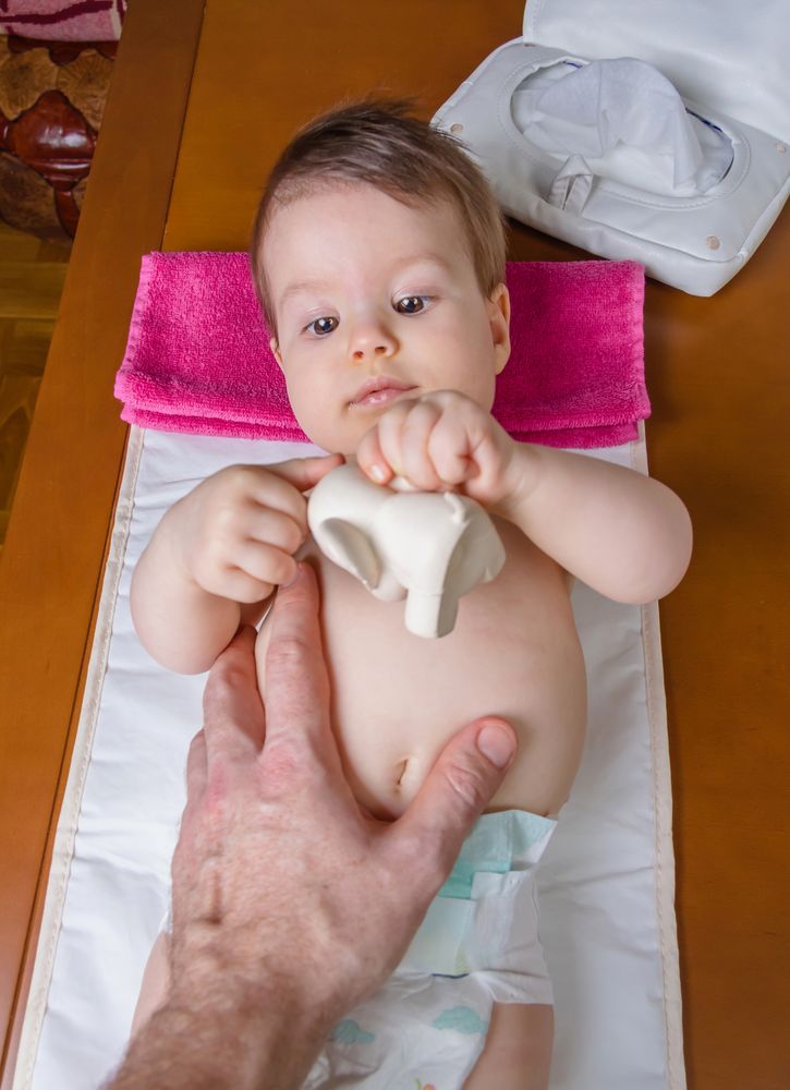 Adorable baby lying playing with a toy with father's hand on belly