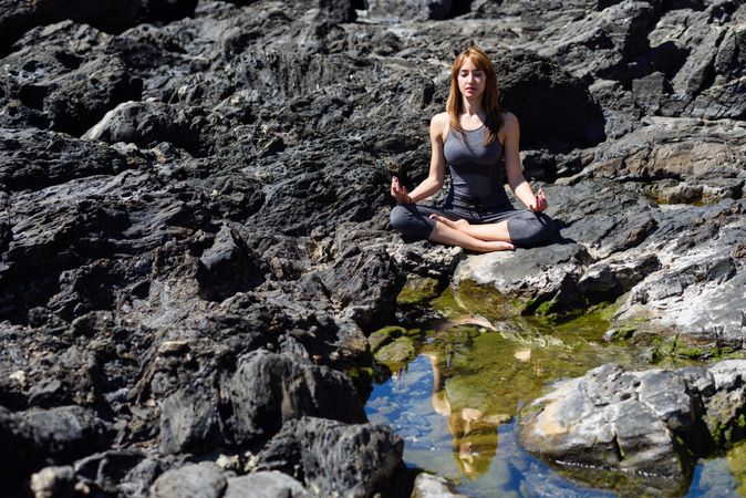Young woman meditating on on rocks outside