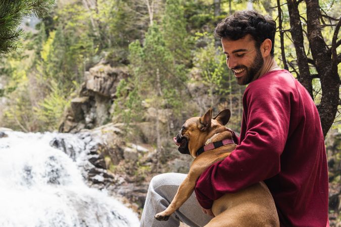 Cheerful traveling man with dog near waterfall in forest