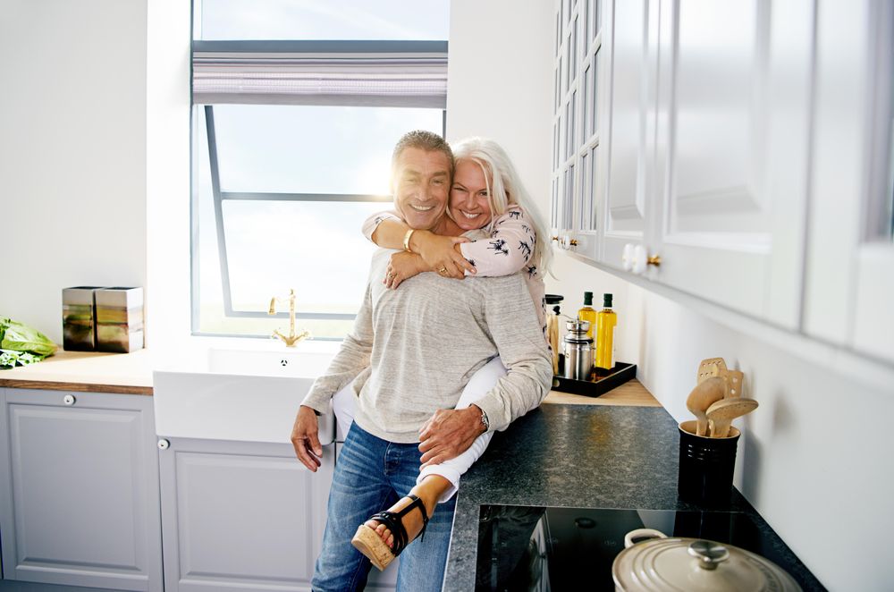 Happy mature couple in kitchen with woman sitting on counter