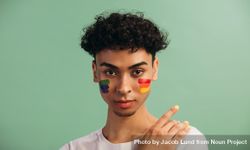 Portrait of a young man with rainbow flag painted on his cheeks. bEl7A4