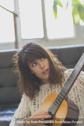 Female in wooly sweater looking at fretboard of guitar 5rRLM5